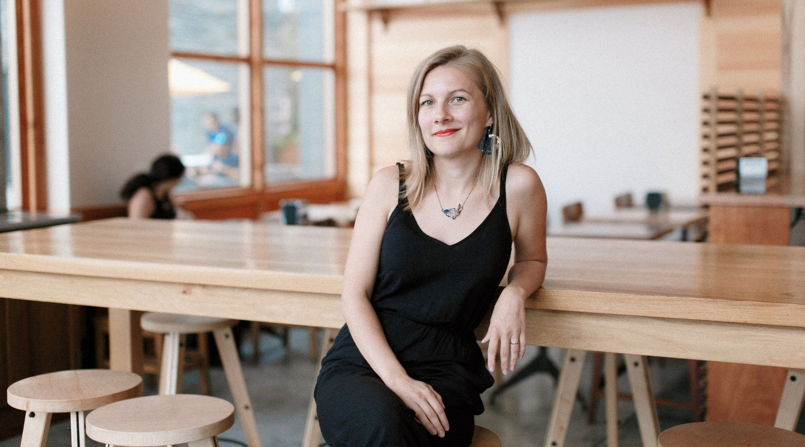 Denisa Piatti sitting in a coffee shop wearing the Seaweed Cluster Necklace in Silver and Ocean Blue, and the Seaweed Pendant Earrings in Silver and Ocean Blue.